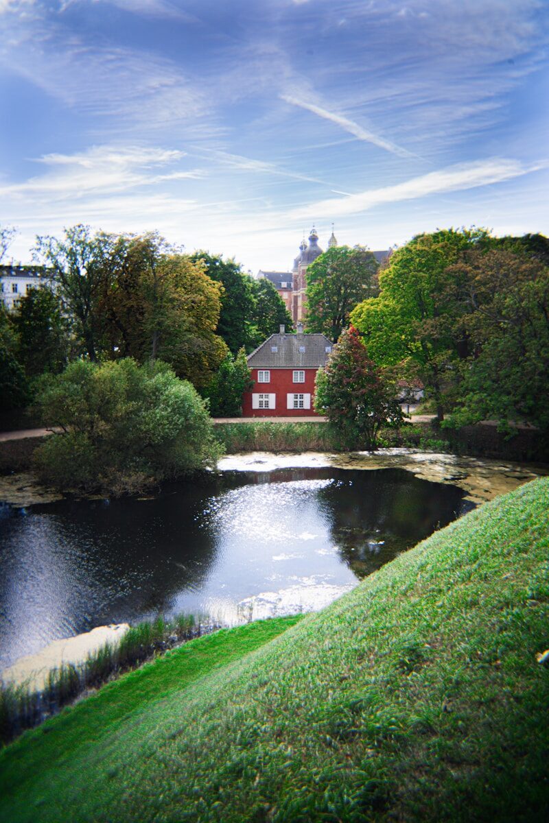 Red house beside a dark pond with trees.